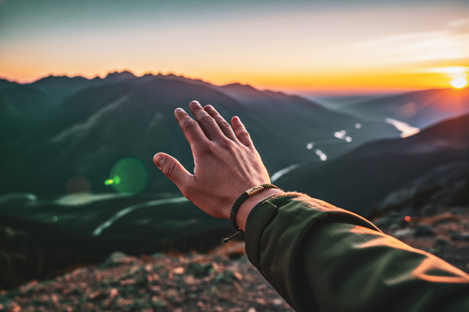 Hand reaching out towards a mountain landscape during sunset